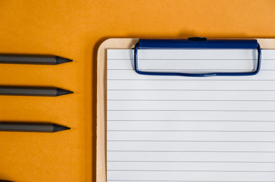 Clip board and pens on an orange background.